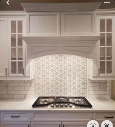 a kitchen with white cabinets and a stove top oven in front of an oven hood