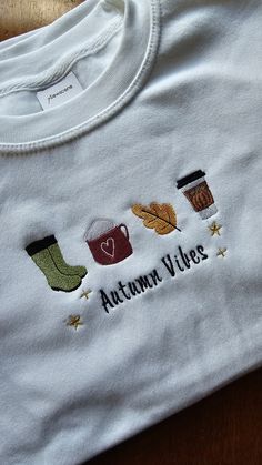 an embroidered t - shirt that says autumn vibes with coffee and boots on it