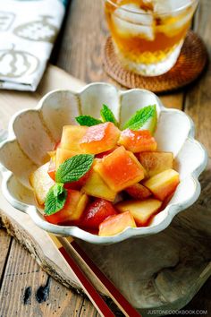 a white bowl filled with sliced fruit next to a glass of tea on top of a wooden table