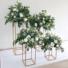 three gold plant stands with white flowers and greenery