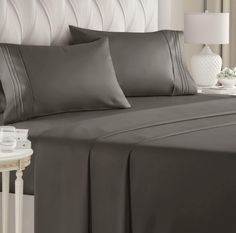 a bed with grey sheets and pillows on it