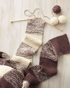 a knitted scarf and two skeins of yarn on a wooden surface with knitting needles