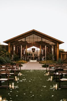 an outdoor wedding venue with wooden chairs and white petals on the grass, lit by candles