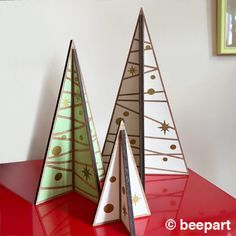 three paper christmas trees sitting on top of a red table next to a framed picture