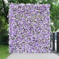 purple flowers are growing on the side of a wall in front of a park bench