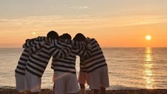 three men standing on the beach with their arms around each other as the sun sets