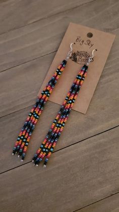 a pair of beaded earrings sitting on top of a wooden table next to a piece of paper