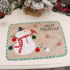 a christmas themed placemat with a snowman on it next to a potted tree