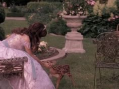 a woman in a wedding dress kneeling down next to a baby deer on a bench