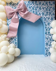 a blue door surrounded by white balloons and pink bow on the top, in front of a wall