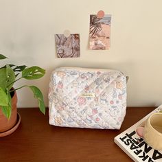 a white purse sitting on top of a wooden table next to a potted plant