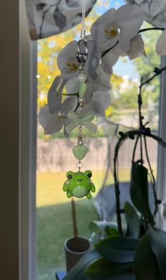 a green frog mobile hanging from a window sill next to a potted plant