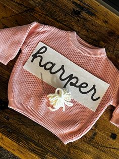 a pink sweater with the word harper on it sitting on top of a wooden table