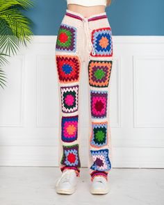 a woman standing in front of a plant wearing colorful crochet pants