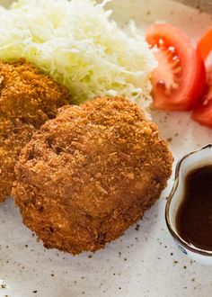 two fried chicken patties with coleslaw and tomato on the side, next to a small bowl of ketchup