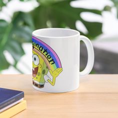 a white coffee mug sitting on top of a wooden table next to a book and plant