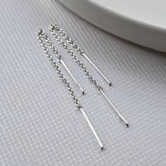 four pairs of silver chain earrings on a white table with a plate in the background