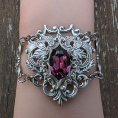 This unique Amethyst bracelet is made with sterling silver plated brass vintage stampings that form a gothic/fantasy look. The center 16x11mm stone is a vintage Swarovski crystal (no longer in production). The bracelet measures 2" tall and 7.5" long, which will fit most women's wrists. I offer two options for the closure:1. A steel slider chain that is easy to adjust and secure.2. A sterling silver plated brass cable chain with a lobster claw closure. If you need longer chain, then please let me Mystical Silver Jewelry With Intricate Design, Silver Gothic Gemstone Jewelry, Gothic Gemstone Jewelry For Collectors, Gothic Collectible Gemstone Jewelry, Collectible Gothic Gemstone Jewelry, Ornate Silver Hand Cast Jewelry, Vintage Silver Amethyst Bracelets, Silver Gothic Collectible Jewelry, Collectible Silver Gothic Jewelry