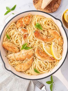 a skillet filled with pasta and shrimp, garnished with lemon wedges