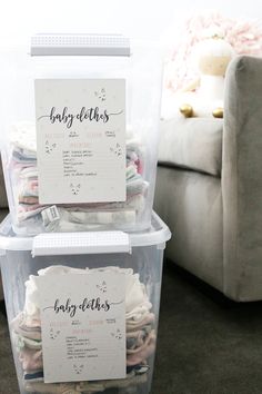 two plastic containers filled with baby clothes sitting on top of a floor next to a couch