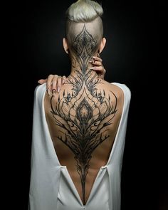 the back of a woman's neck with an intricate tattoo design on her body