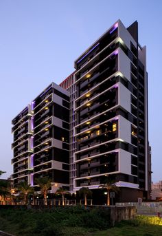 a very tall building with some lights on it's sides in the evening time