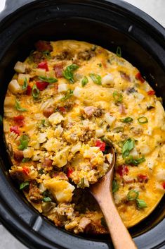 a wooden spoon in a black crock pot filled with eggs and sausage, garnished with green onions