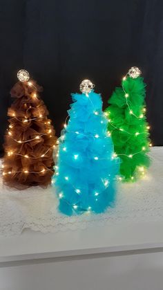 three brightly colored christmas trees on a white surface with lights in the shape of pine cones