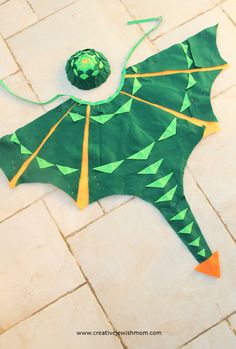 a green dragon kite sitting on top of a white tile floor next to a ball