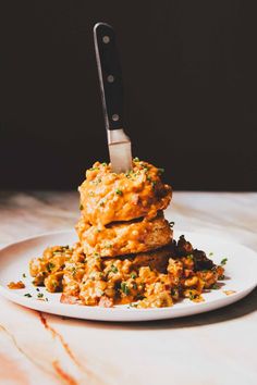 a stack of food sitting on top of a white plate with a knife sticking out of it