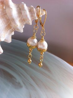 In a minimalist style, a freshwater pearl in a gold-plated scalloped cup and a suspended golden pearl. Gold earrings composed of 9.5 mm freshwater pearls in a 10 mm scalloped cup. A gold-plated bead is suspended. Gold plated back lever earrings. They measure 5.5 cm or 2 and a quarter inches, 2 and a quarter inches from the top of the hooks to the bottom. Earrings with quality freshwater pearls in a minimalist design but with chic that you can wear in a formal evening or every day, plus the delivery is free. Gold Brass Jewelry With Pearl Charm, Gold Jewelry With Pearl Charm In Brass, Delicate Handmade Gold Pearl Earrings, Gold Dangle Jewelry With Pearl Drop, Graceful Gold Jewelry With Pearl Charm, Delicate Yellow Gold Pearl Earrings With Charm, Dainty Handmade Gold Pearl Earrings, Gold Dangle Pearl Earrings With Pearl Chain, Classic Gold Jewelry With Pearl Drop