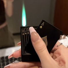 a woman holding two cards in front of a laptop computer with a lit match between her fingers