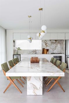 a marble dining table surrounded by green chairs in a white kitchen with gold accents and pendant lights