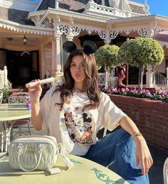 a woman sitting at an outdoor table with mickey mouse ears on her head holding a toothbrush