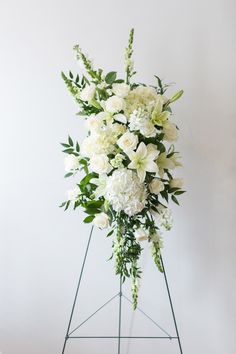 a white flower arrangement on a green stand against a white wall in the corner of a room