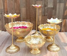 three brass bowls with flowers in them on a table top next to two candlesticks