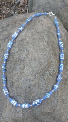 a blue and white beaded necklace sitting on top of a rock