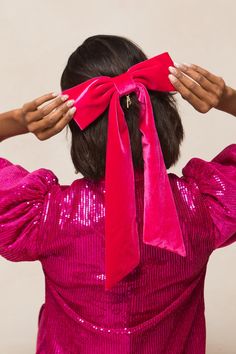 a woman wearing a pink dress with a red bow on her head and hands behind her head