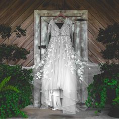 a wedding dress hanging in front of a window with greenery around it and an open door