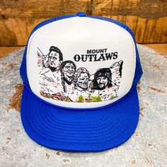 This exclusive trucker hat design from BiggieTexas features the "Mount Rushmore of Outlaw Country music": Willie Nelson, Waylon Jennings, Kris Kristofferson, and Johnny Cash.  This hat fits slightly smaller than our regular trucker hats. These adjustable snapbacks size up and down to fit most small to regular size adults, as well as youths. * Size: Small Adult / Youth * Crown height: 3-1/2", or Mid-Crown * Hat type: Structured * Snap type: Plastic * Trim: Braided Rope * Brim style: Curved This d Flat Brim Trucker Hat For Fan Gear, One Size Flat Bill Trucker Hat For Fan Gear, Adjustable Flat Bill Trucker Hat For Fan Gear, Fan Merchandise Snapback Trucker Hat, Adjustable Flat Bill Hats For Fan Merchandise, Adjustable Flat Bill Hat For Fan Merchandise, Trucker Baseball Cap For Fan Gear, Fan Merchandise Trucker Hat With Flat Bill, Flat Bill Trucker Hat For Fan Merchandise