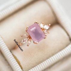 an engagement ring with a pink stone surrounded by white and clear stones in a box