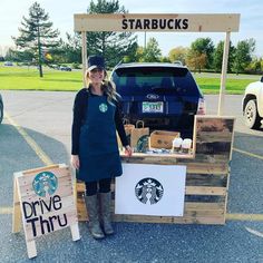 a woman standing in front of a table with starbucks signs on it and a truck behind her