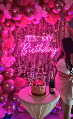 a woman standing next to a table with a cake on it and balloons in the background