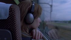 a woman wearing headphones looking out the window on a train at dusk or dawn