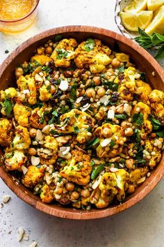 a wooden bowl filled with roasted cauliflower and green beans next to lemon wedges