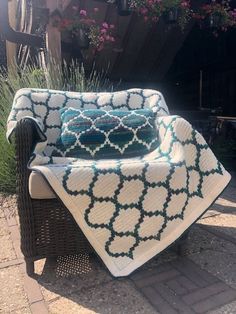 a chair with a blanket on it sitting in front of some flowers and potted plants