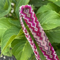 a pink and white bracelet sitting on top of a green plant