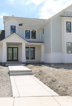 a large white house sitting in the middle of a dirt field next to a sidewalk