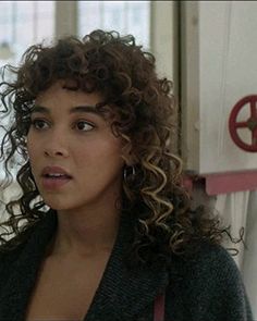 a woman with curly hair standing in front of a door and looking off to the side