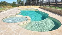 a large swimming pool surrounded by stone steps and fenced in area with hot tub